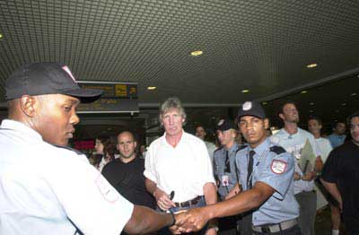 A nervous looking Roger is ushered through the airport by security guards